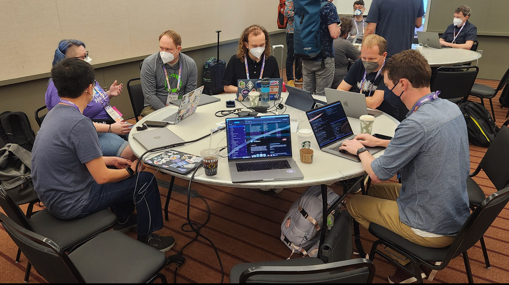 Image of a round table of people talking and working at computers during our sprints.