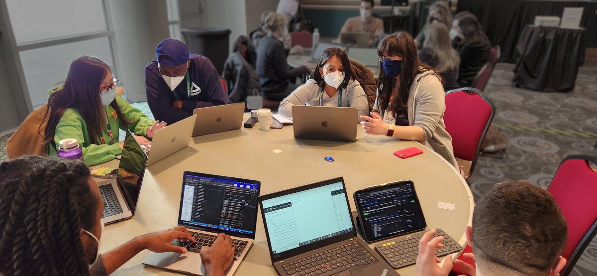Image showing people at laptops sitting around a round table wearing masks during our PyCon 2023 mentored sprint. 